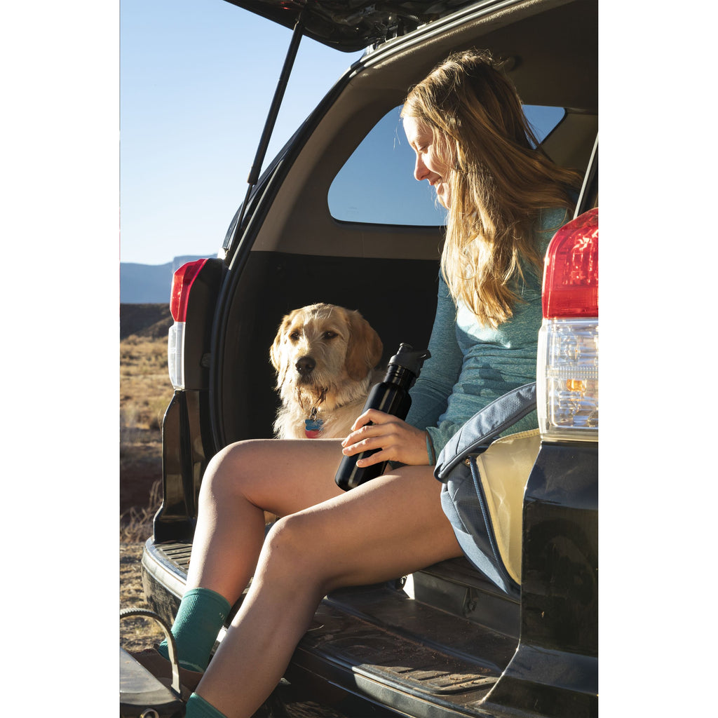 Wasserflasche wird von einer Frau gehalten die neben ihrem Hund im Kofferraum ihres Autos sitzt. Eco Edelstahlflasche super für Wasser und Firmendrucke geeignte
